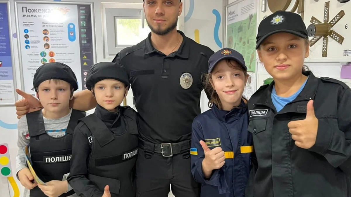 Поліцейський із чотирма дітьми у формі поліції та ДСНС біля навчальних стендів