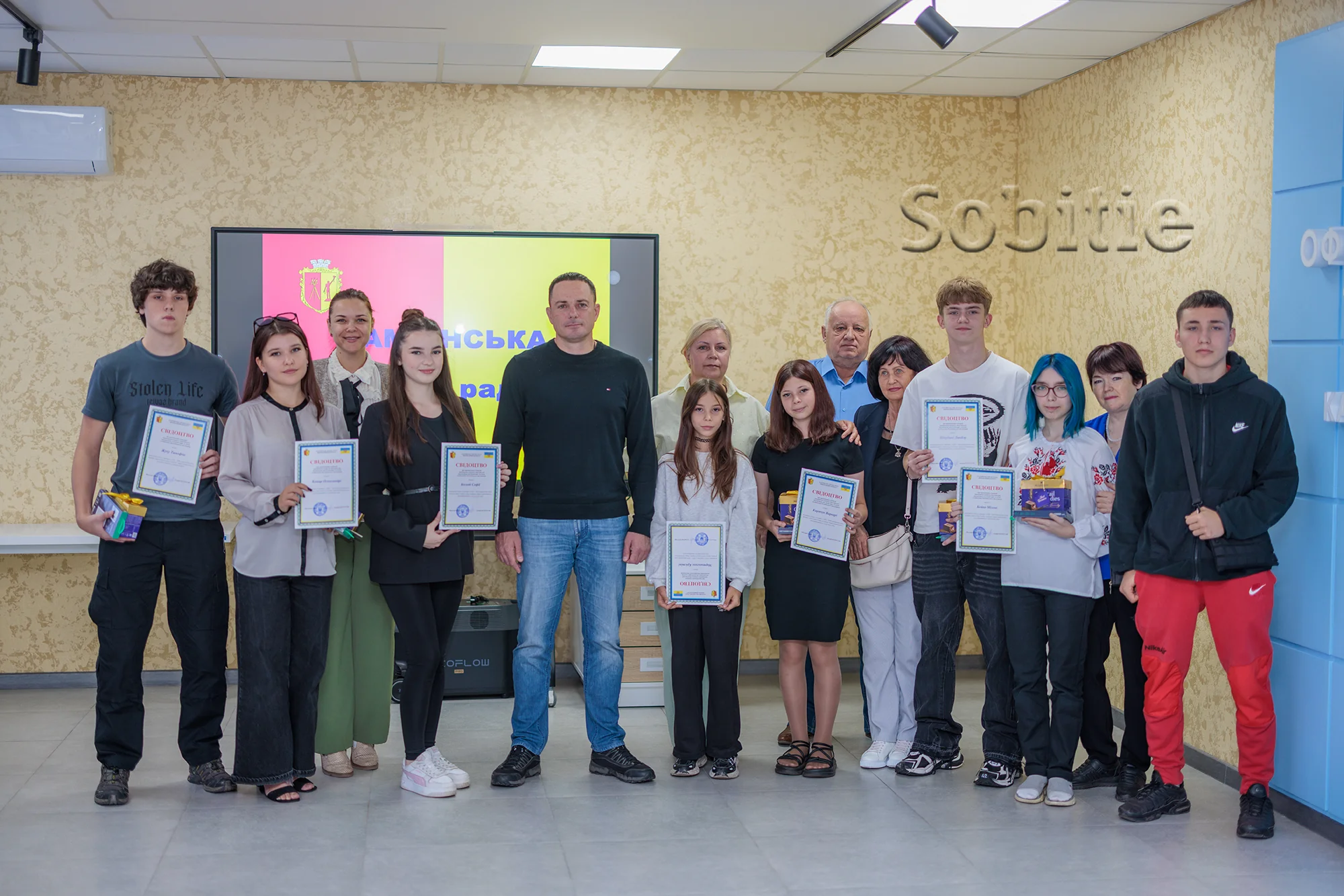 Група підлітків і дорослих з грамотами біля екрана Кам’янської ради