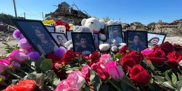 Меморіал з портретами, іграшками та трояндами на тлі зруйнованих будинків